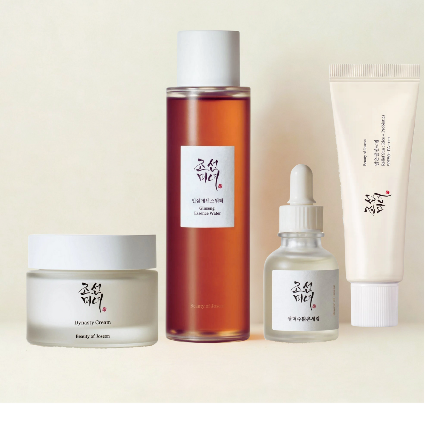 Beauty of Joseon skincare essentials collection featuring Dynasty Cream in a frosted jar, Ginseng Essence Water in a tall amber bottle, Glow Serum in a dropper bottle, and Relief Sun SPF cream in a soft tube, arranged neatly on a beige background